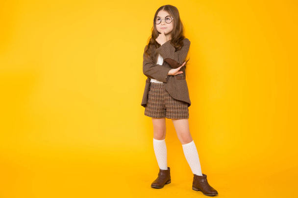 Thoughtful cute little girl posing against yellow background  - Фото, зображення