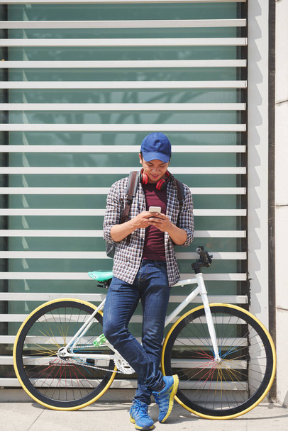 Młody człowiek z rowerów stojących na zewnątrz i SMS-y - Zdjęcie, obraz