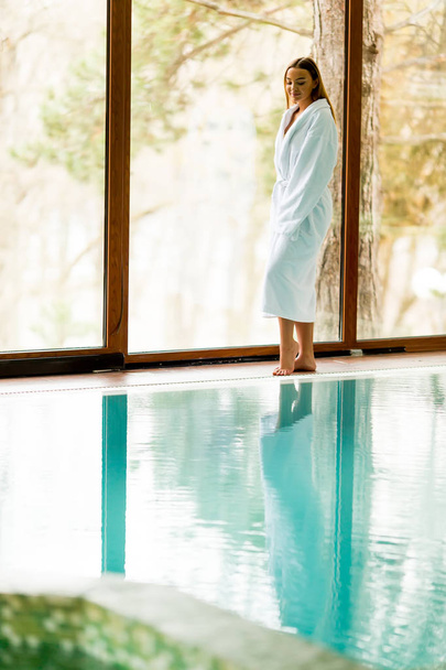 Pretty young woman relaxing by swimming pool in spa center - Foto, Bild