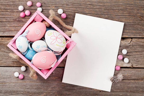 Easter eggs in box and greeting card on wooden table. Top view with space  - Photo, Image