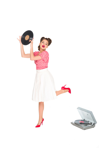 Emotionale Frau in Pin-up-Kleidung mit Schallplatte in den Händen, die neben einem Phonographen steht, isoliert auf weiß - Foto, Bild