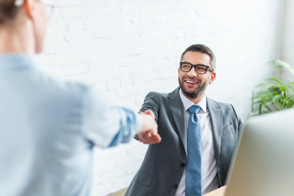 businessman shaking hand of colleague while sitting at workplace - Photo, Image