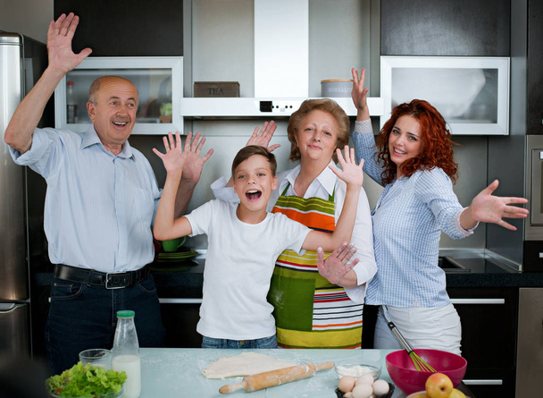 Grand-parents, parents et enfants cuisinent dans la cuisine, rient, s'amusent les mains en l'air
 - Photo, image
