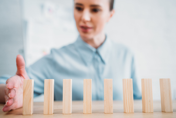 close-up shot of attractive businesswoman assembling wooden blocks in row on worktable, dominoes effect concept - Foto, imagen