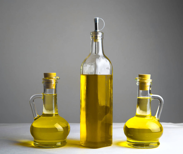 drie olijfolie transparante glasflessen met kurken op witte tafel op keuken  - Foto, afbeelding