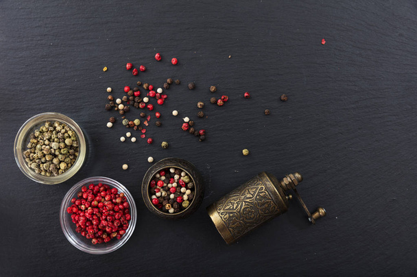 Peppercorns and a bronze pepper mill on black background, top view, copy space - Photo, Image