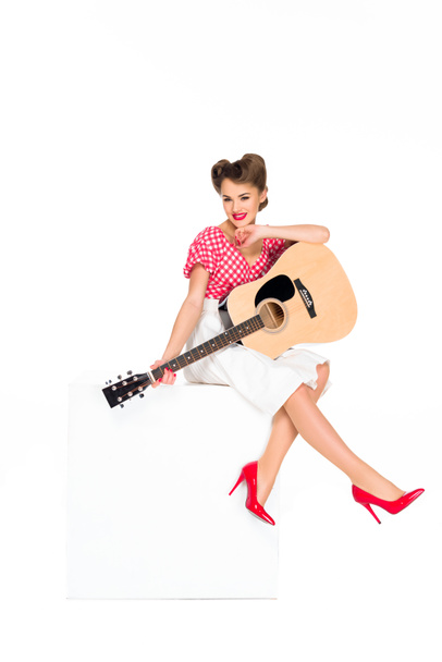 attractive young woman in retro clothing with guitar sitting on cube isolated on white - Photo, Image