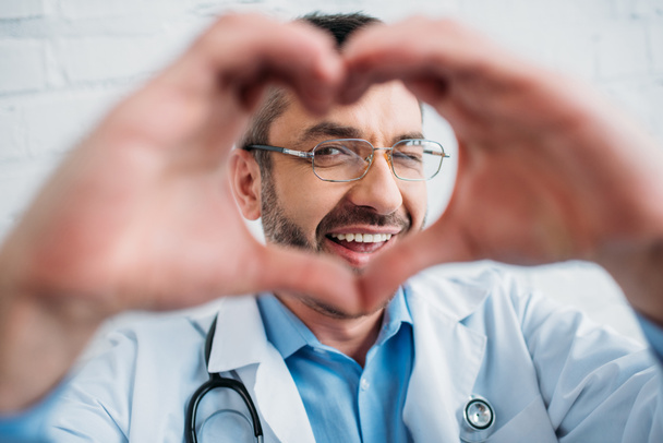 happy handsome doctor showing heart sign with hands - Photo, Image
