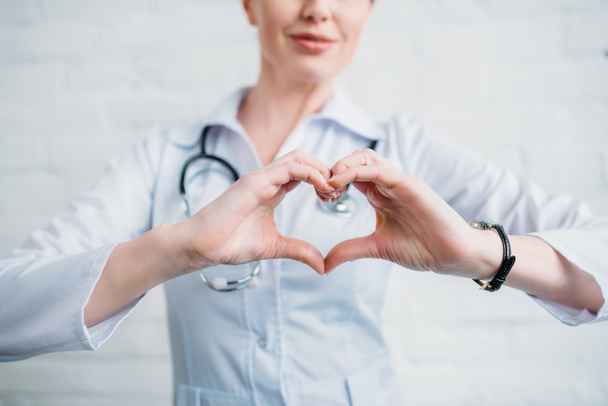 inyección recortada de médico femenino que muestra el signo del corazón con las manos
 - Foto, Imagen