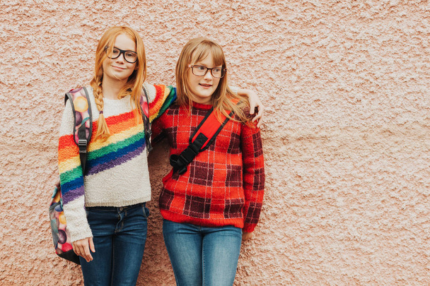 Groep van twee schattige jongen meisjes buitenshuis poseren tegen roze muur, het dragen van bril, school rugzakken en heldere kleurrijke truien, terug naar school concept - Foto, afbeelding