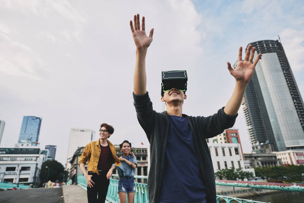 Iloinen teini käyttäen virtuaalitodellisuus kuulokkeet kävellessään ystävien kanssa kaupungin keskustassa, vyötärö-up muotokuva
 - Valokuva, kuva
