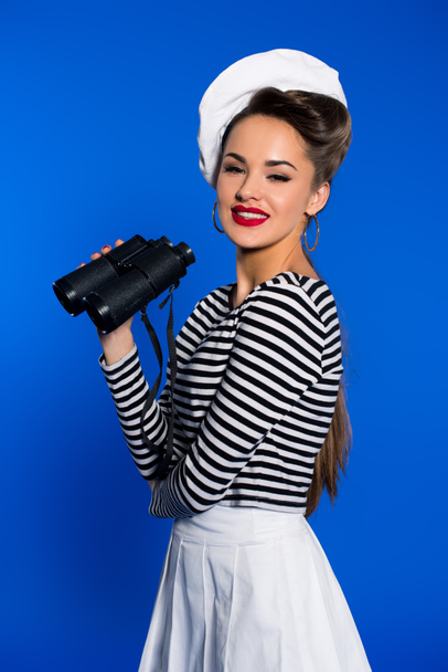 portrait of smiling young woman in retro clothing with binoculars isolated on blue - Foto, Bild