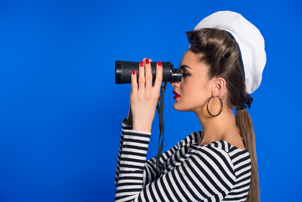 side view of attractive young woman in retro clothing with binoculars isolated on blue - Fotoğraf, Görsel