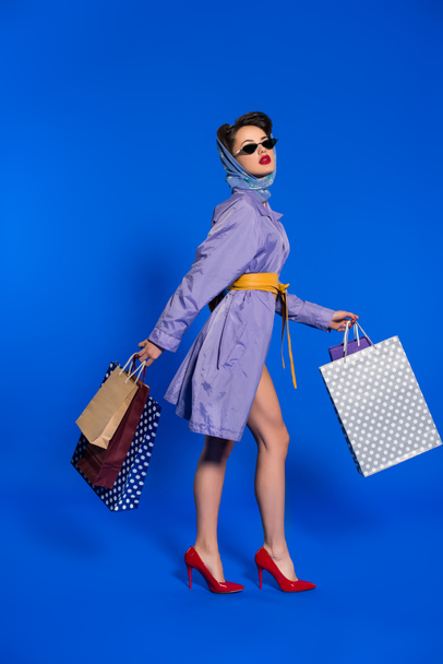 stylish woman in retro clothing with shopping bags isolated on blue - Foto, imagen
