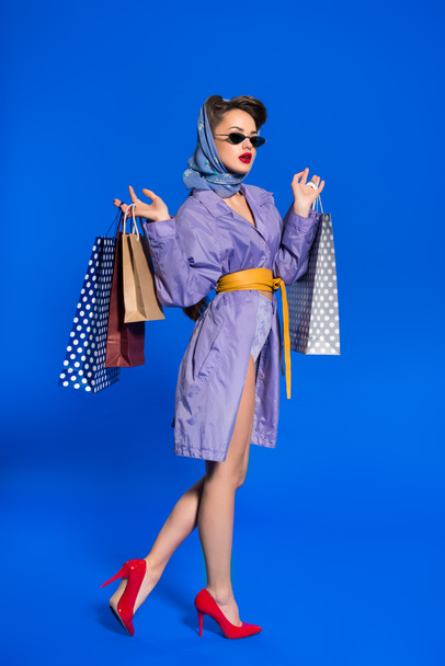 stylish woman in retro clothing with shopping bags isolated on blue - Foto, Bild