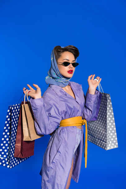 portrait of stylish woman in retro clothing with shopping bags isolated on blue - Fotó, kép