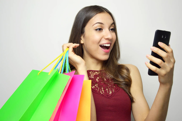 Woman shopping online concept. Attractive woman with smart phone and shopper bags in her hands looking to the side at your brand or product on white background. Copy space. - Photo, Image