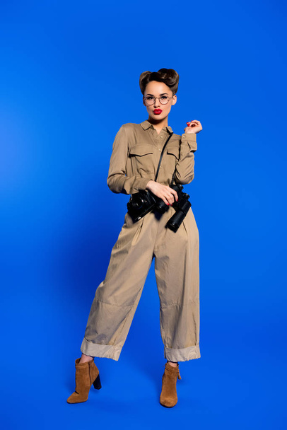 fashionable young woman in retro clothing with photo camera and binoculars isolated on blue - Photo, Image