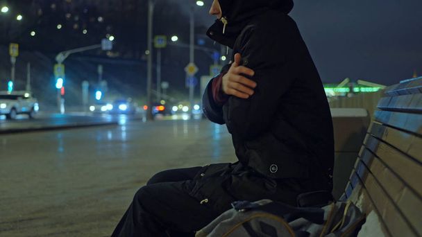 uomo nel cappuccio si riscalda sulla panchina di notte in strada durante il vento nevoso
 - Foto, immagini