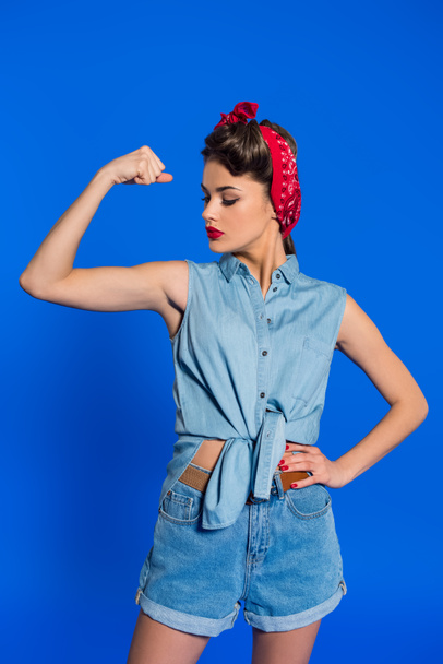 retrato de mujer joven vestida con ropa retro mostrando músculos aislados en azul
 - Foto, Imagen