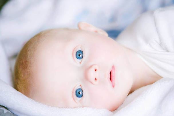 Αξιολάτρευτο μωρό αγόρι σε λευκό ηλιόλουστη κρεβατοκάμαρα. Νεογέννητο παιδί ξεκούραστη στο κρεβάτι. Φυτώριο για μικρά παιδιά. Κλωστοϋφαντουργίας και της κρεβάτια για τα παιδιά. Οικογένεια το πρωί στο σπίτι - Φωτογραφία, εικόνα