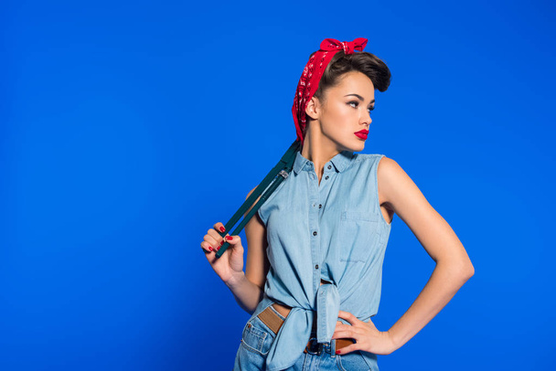fashionable young woman in pin up style clothing with wrench isolated on blue - Foto, immagini