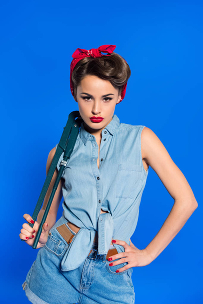fashionable young woman in pin up style clothing with wrench isolated on blue - Fotoğraf, Görsel