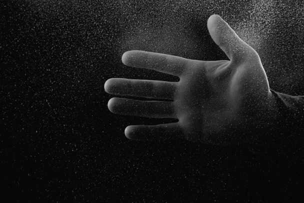 暗闇の中で曇りガラスを通して手のひらを示す人のショットをトリミング  - 写真・画像