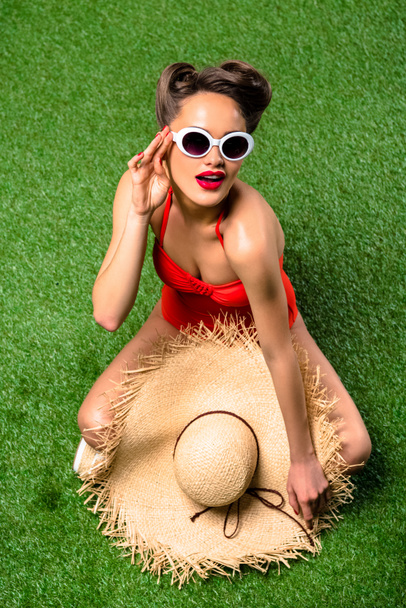 overhead view of beautiful woman in swimming suit with straw hat resting on green lawn - Fotografie, Obrázek