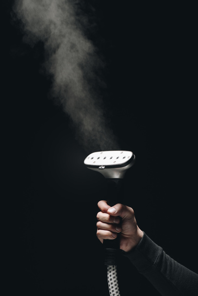 close-up partial view of person holding garment steamer with steam on black - Photo, Image