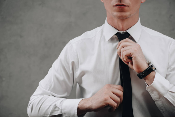 cropped shot of businessman adjusting necktie on grey - Foto, afbeelding
