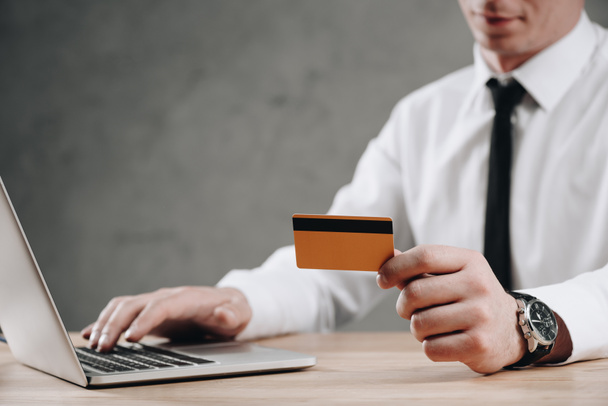 обрізаний знімок бізнесмена, що тримає кредитну картку і використовує ноутбук
 - Фото, зображення