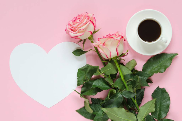 Two pink blooming fresh rose flower with cup of coffee and paper heart for text on pink background - 写真・画像