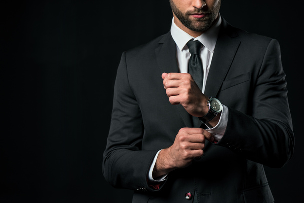 abgeschnittene Ansicht eines Geschäftsmannes in Jacke mit Armbanduhr, isoliert auf schwarz - Foto, Bild