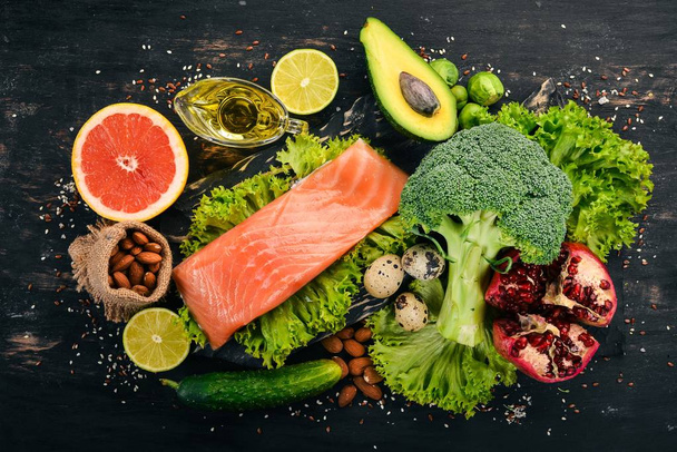 Healthy food. Fish salmon, avocado, broccoli, fresh vegetables, nuts and fruits. On a black background. Top view. Copy space. - 写真・画像