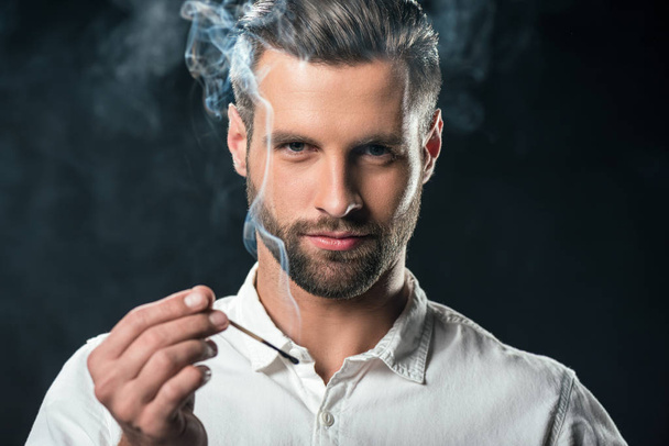handsome businessman holding match with smoke, isolated on black - Foto, afbeelding