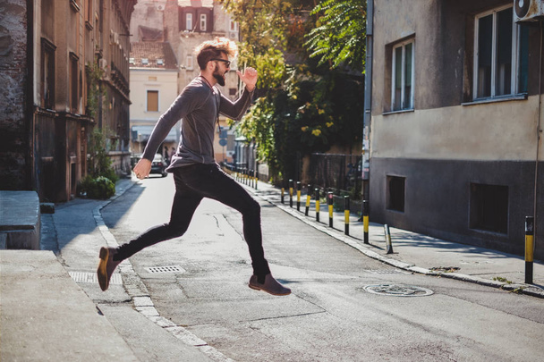 Ekstatyczny hipster skacze na ulicy z jego otwarte usta - Zdjęcie, obraz