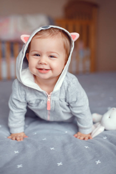 かわいい白人金髪笑みを浮かべて赤ちゃんの愛らしい少女灰色パジャマの寝室で狐猫動物フード付きの肖像画。自然な感情の表情。幸せな子供時代のライフ スタイル コンセプト - 写真・画像
