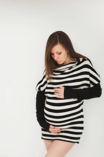 Красива мода вагітна молода щаслива брюнетка в смугастій чорно-білій сукні з великим животом. Вагітність, батьківство, сім'я, материнство, батьки, діти, люди та концепція очікування
. - Фото, зображення