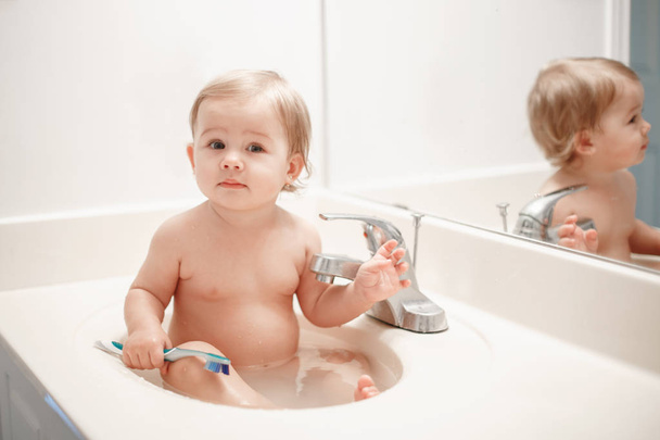 Portret ładny Kaukaska Blondynka śmieszne dziecko dziewczyna chłopiec siedzi w umywalka umywalnia z wody. Dziecko szczotkowanie zębów. Koncepcja szczęśliwe dzieciństwo zdrowe. Codziennie do domu rodziny słodka chwila - Zdjęcie, obraz