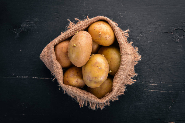 Raw potatoes on a black wooden background. Cooking. Free space for text. Top view. - Foto, Imagen