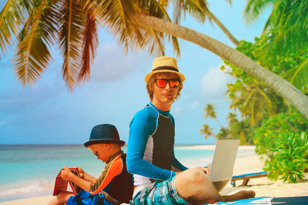 vader met laptop, zoon kijken touchpad op strand - Foto, afbeelding