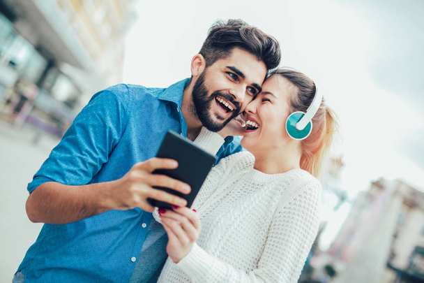 Hermosa pareja joven caminando por la calle y escuchando música con tabletas y auriculares
.  - Foto, imagen