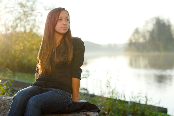 Teenage girl resting by river at golden hour - Фото, зображення