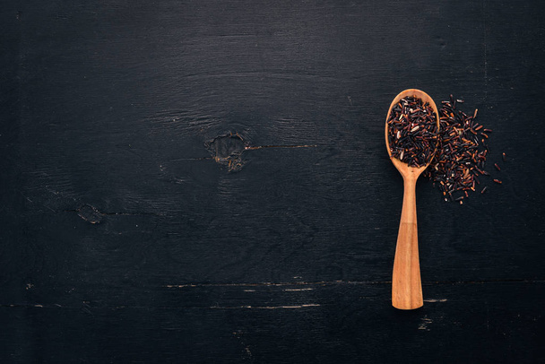 Black wild dry rice on a spoon. On a wooden background. Top view. Copy space. - Фото, изображение