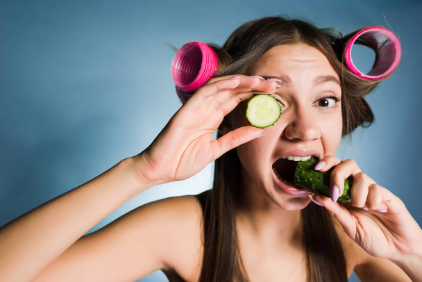 woman with curlers on her head eating cucumber - Foto, Imagen
