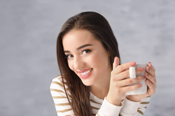 Hermosa mujer sonriente con taza de café sobre fondo gris
 - Foto, Imagen