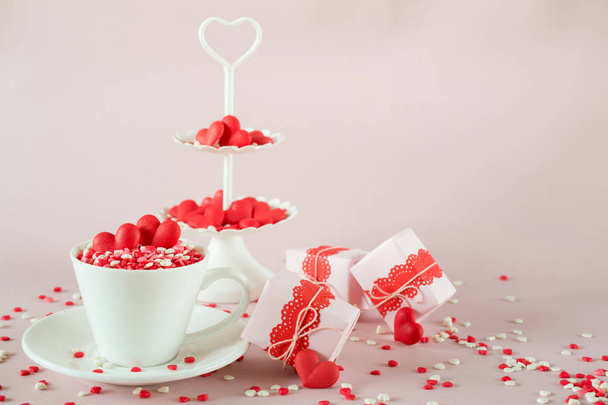 Festive background.  Coffee cup, white two tier serving tray full of multicolor sweet sprinkles sugar candy hearts and packing Valentine's  Day gifts  Love and Valentine's day concept.  - Foto, Bild