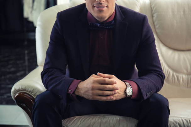 Young man in elegant suit sitting on sofa at menswear store - Foto, Imagem