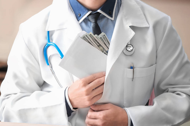 Doctor putting envelope with money in pocket, closeup. Corruption concept - Фото, изображение